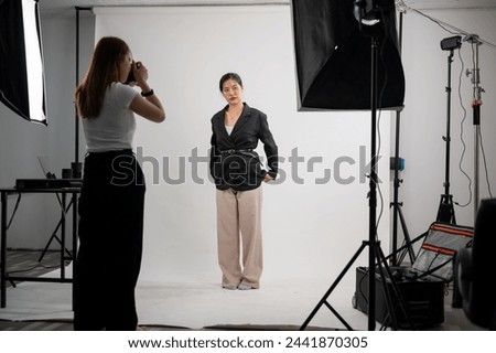 An attractive Asian female model is posing for a photographer in a modern fashion studio with professional lighting equipment. fashion industry, photoshoot backstage