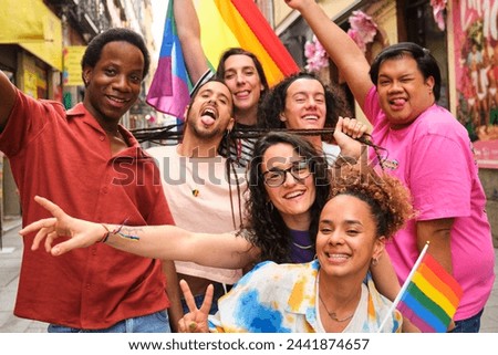 A group of people are posing for a picture, holding rainbow flags at the Pride Parade. Scene is joyful and celebratory.