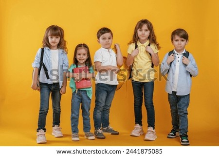 Standing and posing. Kids are together against yellow background.