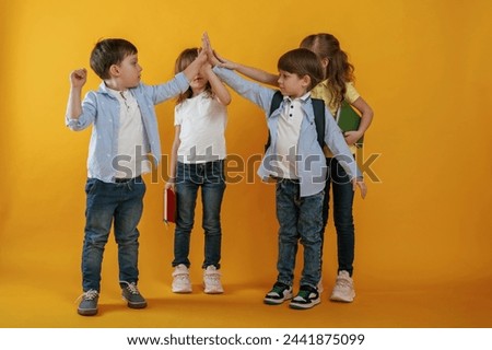 Giving high fives. Kids are together against yellow background.
