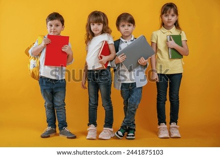 Notepads in hands, conception of education. Kids are together against yellow background.