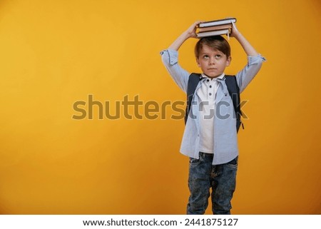 Playing with book, holding it on the head. Little boy is in the studio against yellow background.