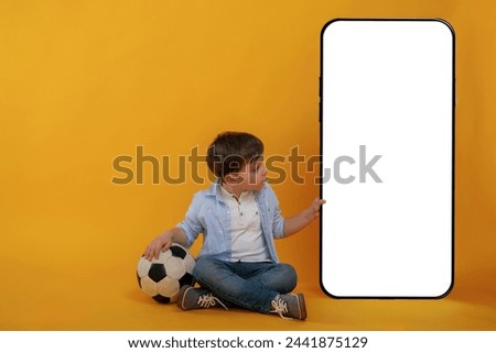 With huge smartphone, copy space place. Little boy is in the studio against yellow background.