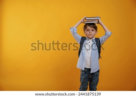Playing with book, holding it on the head. Little boy is in the studio against yellow background.