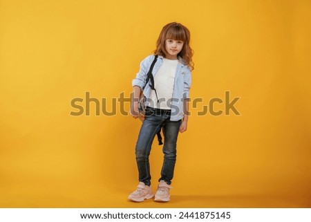 With backpack. Cute little girl is against yellow background.