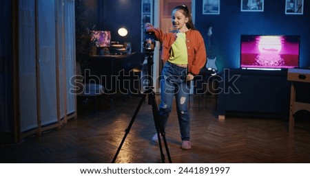 Dolly in shot of kid media star recording trendy dance video clip for social media using cellphone on tripod stabilizer, entertaining audiences. Gen z influencer recording content using smartphone