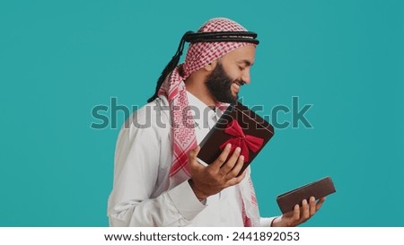 Arab person opening giftbox with ribbon, receiving beautiful present on his birthday. Middle eastern happy guy feeling excited about gift wrapped with box, holiday package.