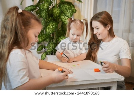 Young mother or babysitter, little daughter, sister teenager girl drawing at table in room. Painting, doing homework, family enjoying leisure at home
