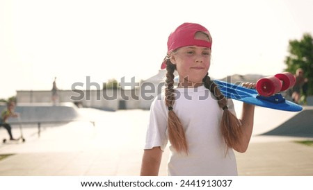 child walk with a skateboard. girl in red cap with a skateboard on the playground portrait. skateboarder child walk outdoors sun glare lifestyle. kid skateboarder to light the skatepark