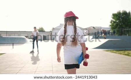 child walk with skateboard. girl in a red cap with a skateboard on the playground portrait. skateboarder child walk outdoors sun glare lifestyle. kid skateboarder lifestyle to the skatepark