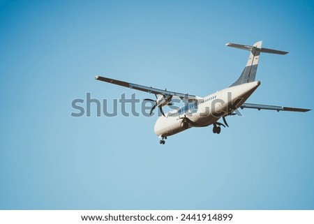 Rear view of an ATR 72 airplane in the clear blue sky. Twin-engine turboprop short-haul regional passenger aircraft. Landing airplane. Blue background. Royalty-Free Stock Photo #2441914899
