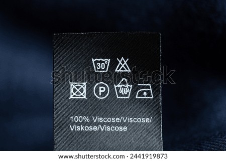 Care label with icons giving information about how to wash, dry and iron the clothing. Black label with white pictogram symbols. Instructions and info about the material of the garment  Royalty-Free Stock Photo #2441919873