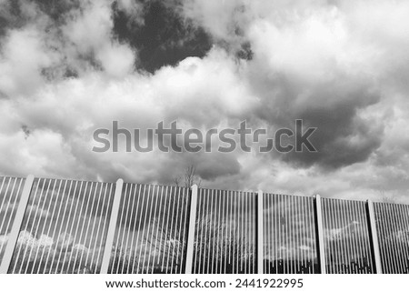 Highway fence, highway noise barrier and beautiful sky with clouds, black and white photo