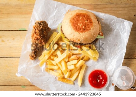 several types of fast food such as hamburgers, french fries, fried chicken and tomato sauce on a wooden table. Royalty-Free Stock Photo #2441923845
