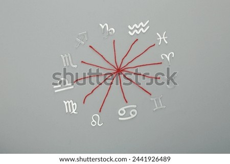 Zodiac compatibility. Signs and red threads on grey background, flat lay Royalty-Free Stock Photo #2441926489