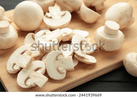 Fresh white champignon mushrooms on cutting board on black background. Royalty-Free Stock Photo #2441939669