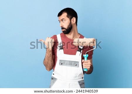 Adult painter man over isolated blue background unhappy and pointing to the side