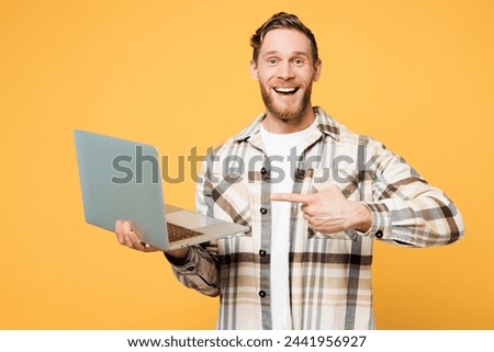 Young surprised Caucasian IT man he wear brown shirt casual clothes hold use work point index finger on laptop pc computer isolated on plain yellow orange background studio portrait. Lifestyle concept