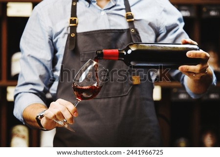 Male sommelier pouring red wine into long-stemmed wineglasses. Royalty-Free Stock Photo #2441966725