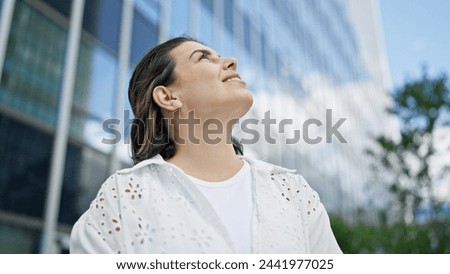 Beautiful young hispanic woman smiling confident looking to the sky in the streets of Stockholm