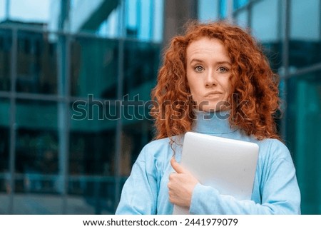 worried young woman graduate with curly red hair biting her lip, holding laptop and excited  about news regarding her job application Royalty-Free Stock Photo #2441979079