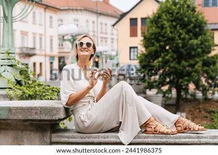 Happy woman using smart phone on the street of european city. Young girl with phone exploring the city. Modern lifestyles of urban people.