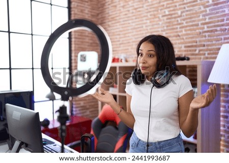 Young arab woman influencer recording herself with smartphone shouting and screaming loud to side with hand on mouth. communication concept.  Royalty-Free Stock Photo #2441993687
