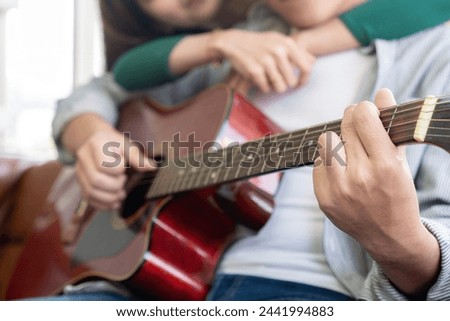 The couple, a young man and woman, are enjoying playing the guitar together at home