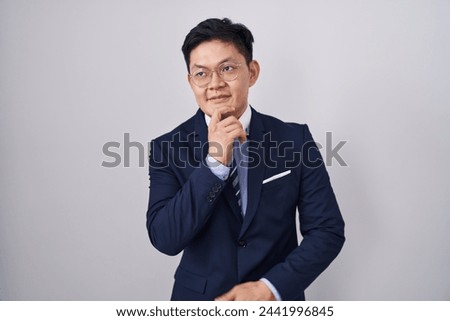 Young asian man wearing business suit and tie with hand on chin thinking about question, pensive expression. smiling and thoughtful face. doubt concept.  Royalty-Free Stock Photo #2441996845
