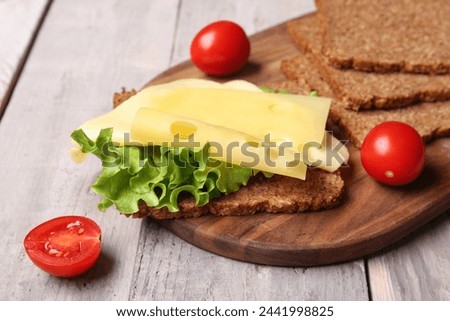 Tasty sandwich with cheese, lettuce and tomatoes on wooden background, closeup Royalty-Free Stock Photo #2441998825
