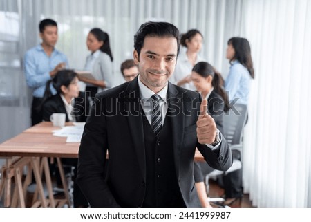 Portrait of happy businessman looking at camera, make approval hand gesture thumb up with motion blur background of business people movement in dynamic business meeting. Habiliment