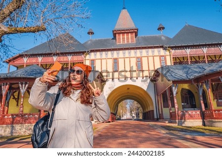 Tourist girl taking selfie photos on her smartphone against buildings on Palic lake, while travelling in Serbia