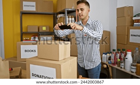 Hispanic man taking photo in warehouse filled with donation boxes and household items.