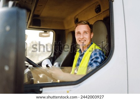 Truck driver job. Logistics - proud driver or forwarder on truck and trailer, on a transshipment point. Transportation service. Royalty-Free Stock Photo #2442003927