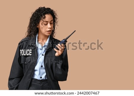 Beautiful young African-American policewoman with radio transmitter on brown background