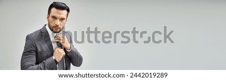 thoughtful man in formal wear adjusting tie on grey background, corporate fashion banner Royalty-Free Stock Photo #2442019289