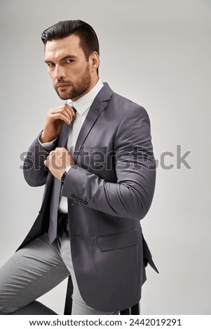 thoughtful businessman in suit adjusting his tie on grey background, corporate style concept Royalty-Free Stock Photo #2442019291
