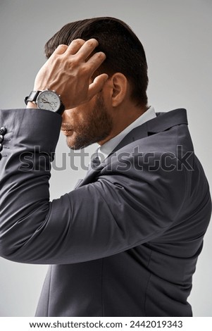 handsome man in formal wear with wristwatch adjusting his hair on grey background, corporate fashion Royalty-Free Stock Photo #2442019343