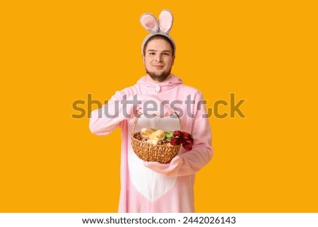 Young man in bunny costume with Easter basket on yellow background