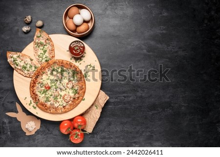 Board of tasty pizza with bunny ears, Easter eggs, paper bunny and tomatoes on black grunge background