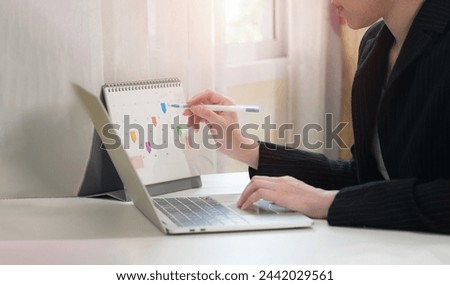 Event planner calendar, agenda, timetable for 2024. Businesswoman using phone to check planner and making notes on desk calendar at her desk in the office. Work planning, event calendar.