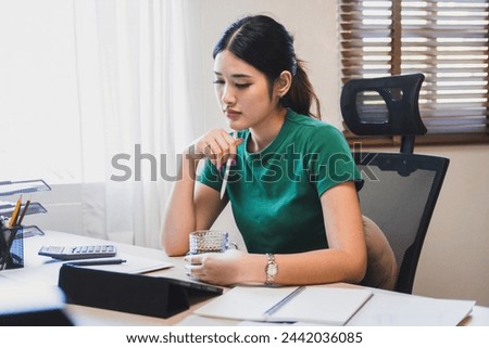 Stressed businesswomanor company employee is sitting at desk with tablet and paper works at workplace thinking, contemplating, and worrying about business matters, plans, and investment outcome and ri Royalty-Free Stock Photo #2442036085