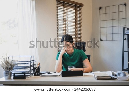 Stressed businesswomanor company employee is sitting at desk with tablet and paper works at workplace thinking, contemplating, and worrying about business matters, plans, and investment outcome and ri Royalty-Free Stock Photo #2442036099