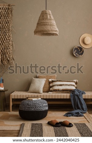 Stylish composition of boho ethno living room with daybed, pillows, hanging decoration, carpet, basket, beige accessories. Home decor. Template.	 Royalty-Free Stock Photo #2442040425