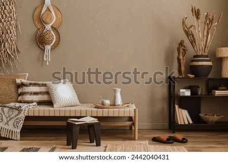 Stylish composition of boho ethno living room with daybed, blak shelf, pillows, hanging decoration, beige accessories. Home decor. Template. Textured wall.	 Royalty-Free Stock Photo #2442040431