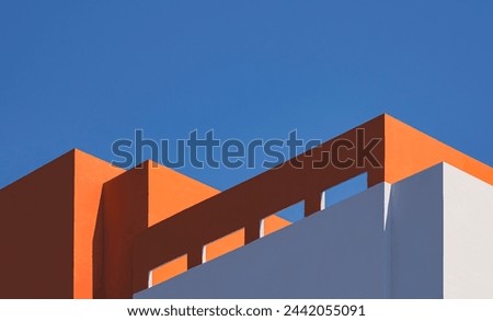 Geometric architecture pattern of high section of modern orange and white building with sunlight and shadow on rooftop surface against blue clear sky background in minimal style, Low angle view Royalty-Free Stock Photo #2442055091