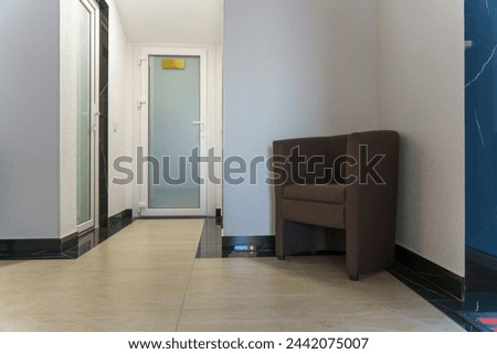 An empty corridor in an office building and upholstered chairs for visitors. White walls and glass doors. A lighted long corridor in a modern business center. Royalty-Free Stock Photo #2442075007