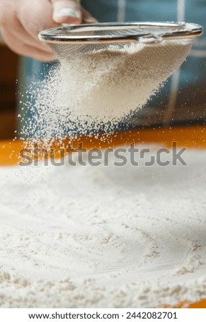 A woman in an apron holds a sieve and sifts flour over the table. Vertical photo