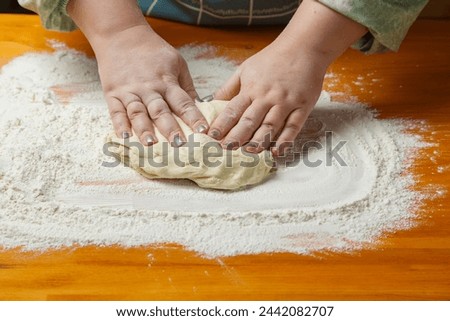 Women's hands knead dough on a table sprinkled with flour. Horizontal photo