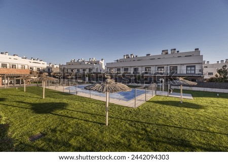Interior area of a block with single-family residential buildings on a beautiful day with blue sky and a central swimming pool with grass and fiber umbrellas